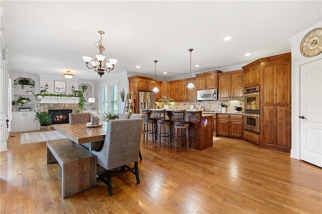 dining area with a fireplace, ornamental molding, a chandelier, and light hardwood / wood-style flooring