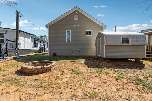 back of house with an outdoor structure, an outdoor fire pit, and a shed