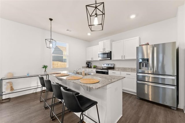 kitchen with appliances with stainless steel finishes, pendant lighting, white cabinetry, light stone countertops, and a center island with sink