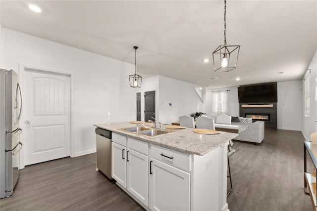 kitchen featuring pendant lighting, sink, appliances with stainless steel finishes, white cabinetry, and a center island with sink