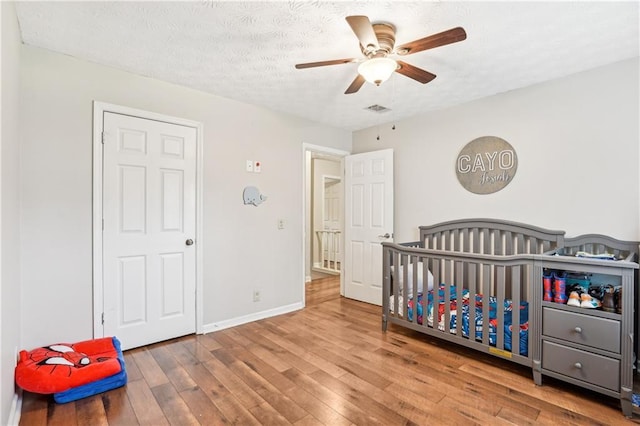 1752 Shadybrook Ct, Lawrenceville, GA 30043 - bedroom with wood finished floors, a textured ceiling, baseboards, a ceiling fan, and a crib