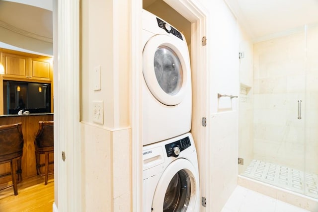 clothes washing area with light hardwood / wood-style floors, ornamental molding, and stacked washer and clothes dryer