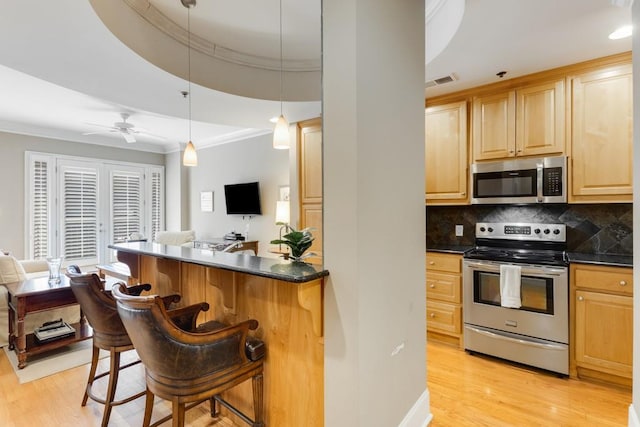 kitchen with a kitchen breakfast bar, light brown cabinetry, appliances with stainless steel finishes, light hardwood / wood-style floors, and ceiling fan