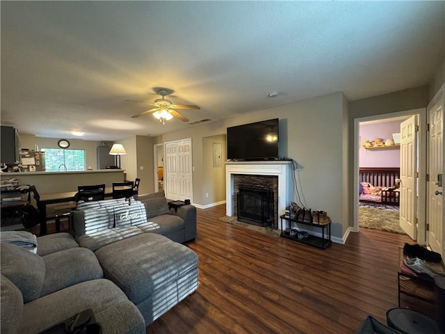 living room with a stone fireplace, ceiling fan, wood finished floors, and baseboards