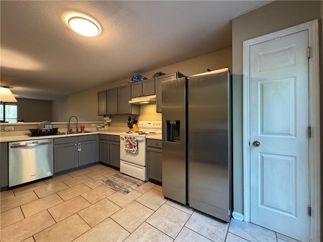 kitchen with under cabinet range hood, light countertops, a sink, stainless steel appliances, and gray cabinetry