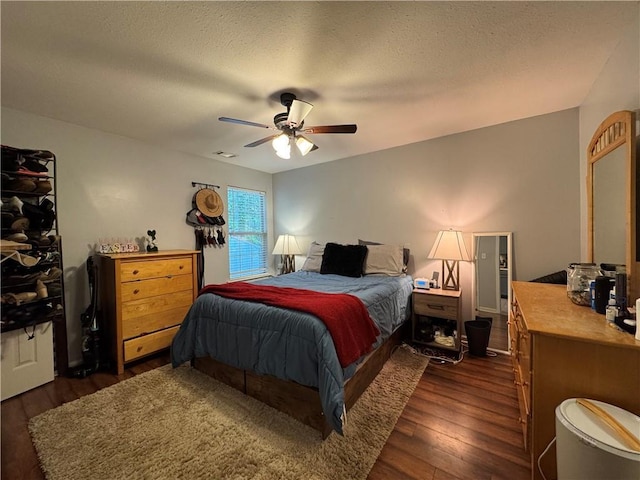 bedroom with dark wood-style flooring, visible vents, ceiling fan, and a textured ceiling