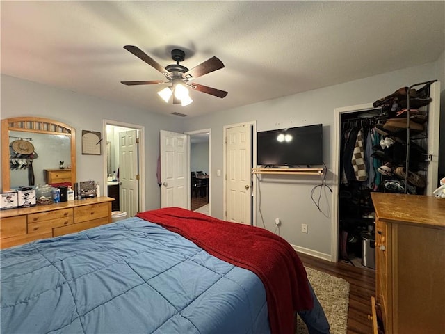 bedroom with two closets, connected bathroom, a ceiling fan, wood finished floors, and baseboards