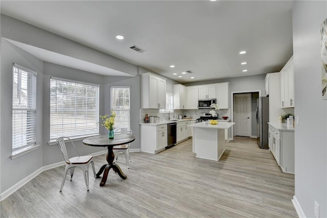 kitchen with light hardwood / wood-style flooring, appliances with stainless steel finishes, white cabinets, and a kitchen island