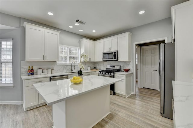 kitchen featuring a kitchen island, appliances with stainless steel finishes, white cabinets, decorative backsplash, and light stone countertops