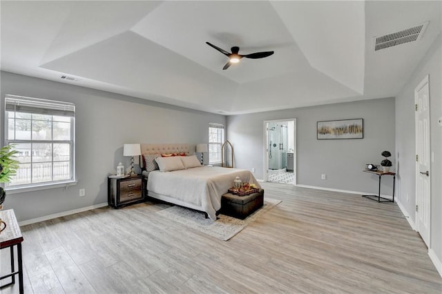 bedroom featuring ensuite bathroom, light wood-type flooring, ceiling fan, and a tray ceiling