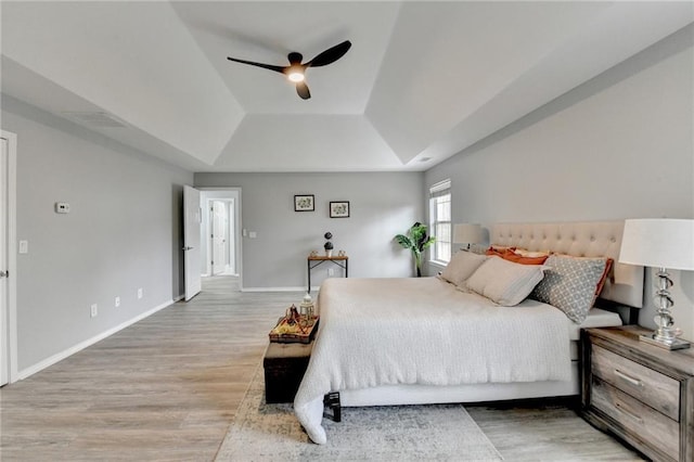 bedroom featuring a raised ceiling, wood-type flooring, and ceiling fan