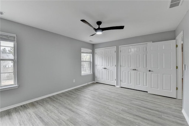 unfurnished bedroom with multiple closets, ceiling fan, and light hardwood / wood-style floors