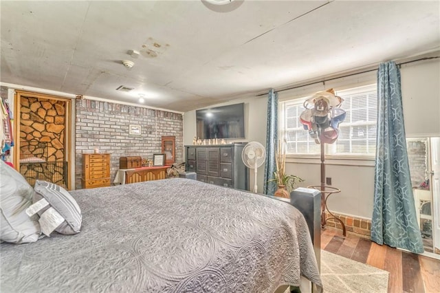 bedroom with brick wall and hardwood / wood-style floors