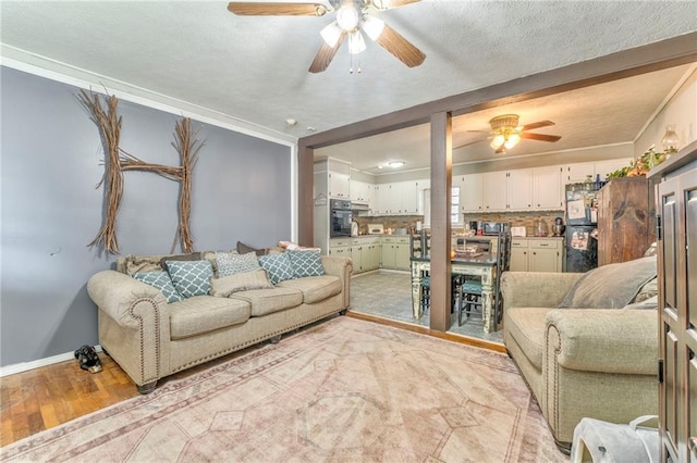 living room with a textured ceiling, light hardwood / wood-style flooring, ornamental molding, and ceiling fan