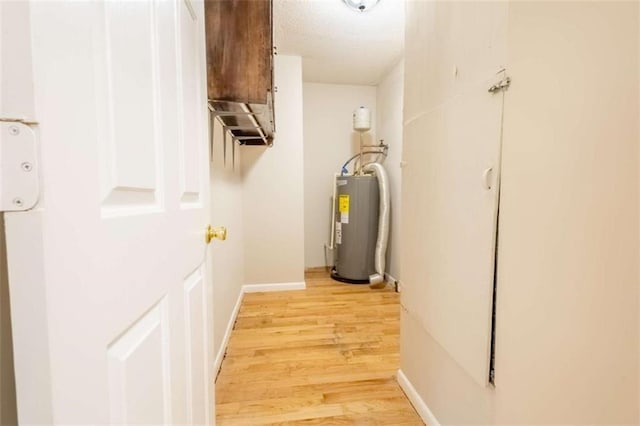 corridor with light wood-type flooring, baseboards, and electric water heater