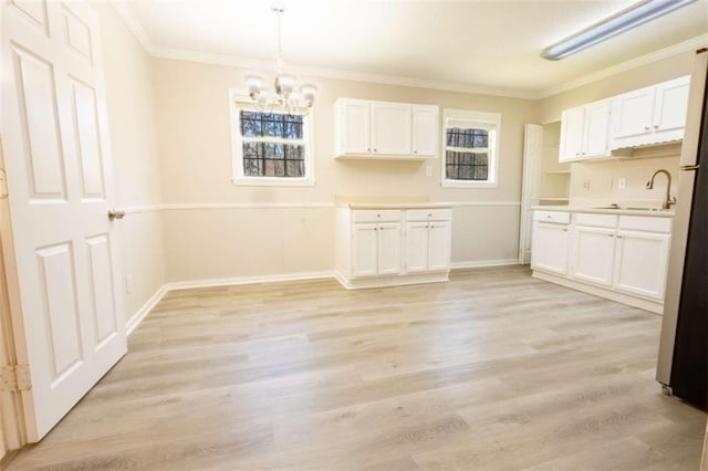 kitchen featuring crown molding, white cabinets, light wood-style flooring, and a sink