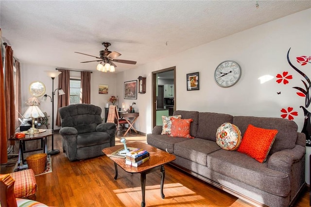 living room featuring hardwood / wood-style flooring, ceiling fan, and a textured ceiling