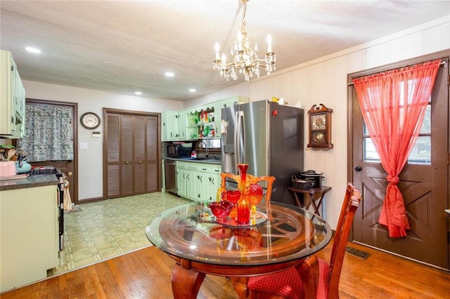 dining space featuring sink, a textured ceiling, an inviting chandelier, and light wood-type flooring