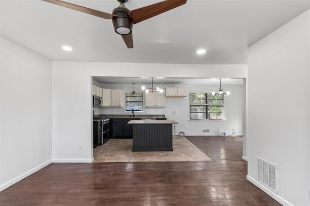 kitchen with dark wood-type flooring, ceiling fan with notable chandelier, appliances with stainless steel finishes, a kitchen island, and decorative light fixtures