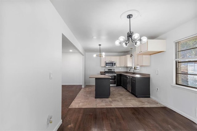 kitchen with sink, a chandelier, a kitchen island, pendant lighting, and stainless steel appliances