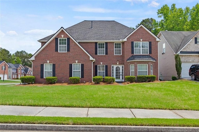 colonial home with brick siding, a front yard, and a shingled roof