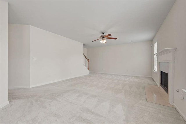 unfurnished living room with a ceiling fan, carpet, a fireplace with raised hearth, and baseboards