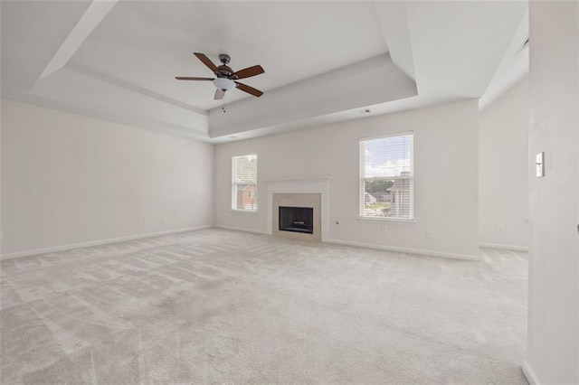 unfurnished living room featuring a raised ceiling, a ceiling fan, baseboards, and carpet floors