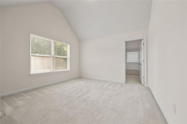 empty room with vaulted ceiling, light carpet, and baseboards