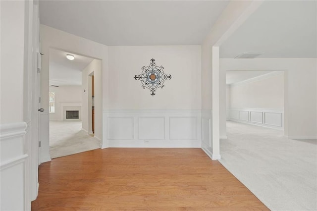 hallway featuring light wood-style floors, wainscoting, and a decorative wall