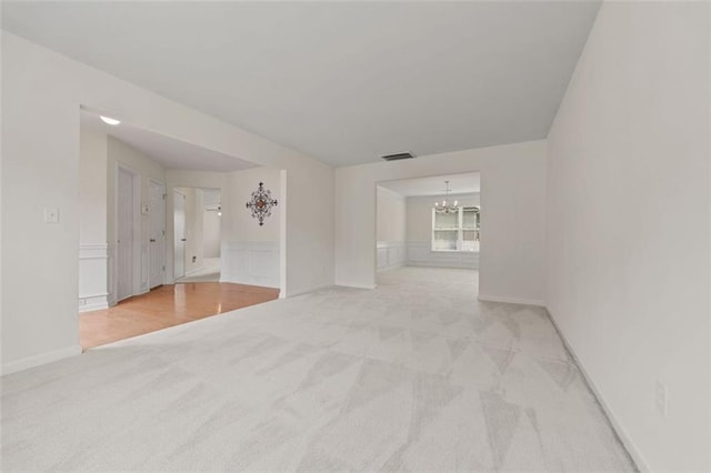 spare room with a chandelier, light colored carpet, and wainscoting