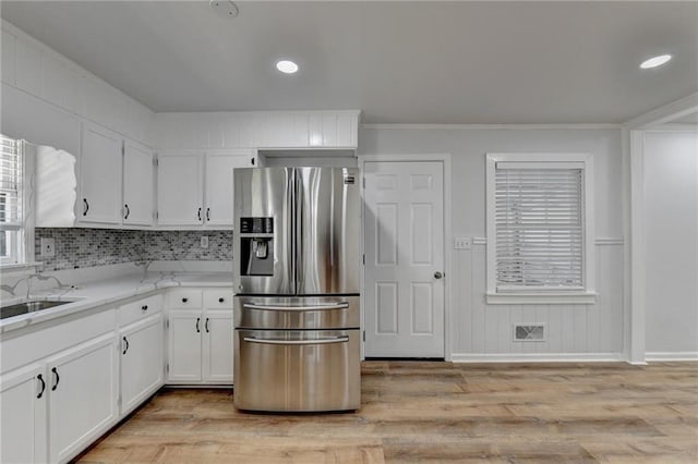 kitchen with backsplash, sink, stainless steel fridge, light wood-type flooring, and white cabinets