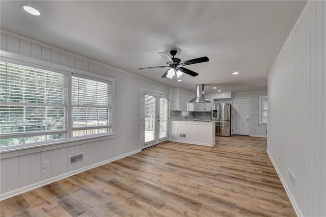 kitchen featuring wall chimney range hood, stainless steel fridge, white cabinetry, light wood-type flooring, and crown molding