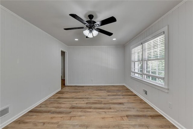 spare room featuring ceiling fan, ornamental molding, light wood-type flooring, and wooden walls