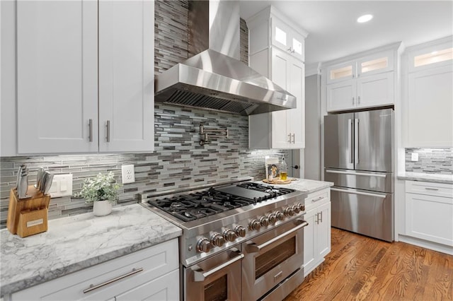 2510 Wood Creek Ct, Dacula, GA 30019 - kitchen with wall chimney exhaust hood, stainless steel appliances, decorative backsplash, white cabinets, and light wood-type flooring