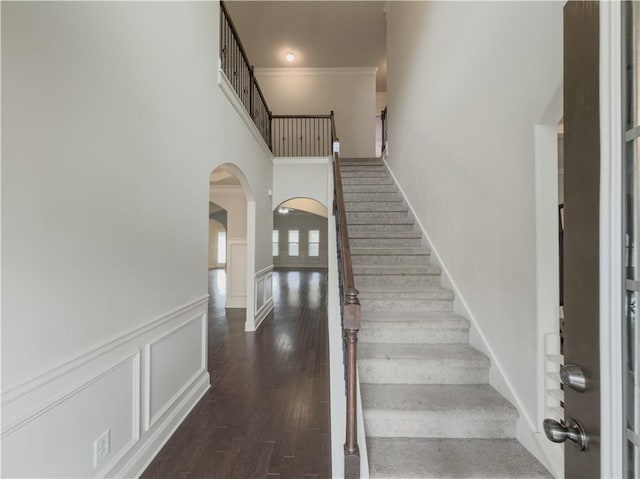 staircase featuring a towering ceiling, hardwood / wood-style flooring, and crown molding