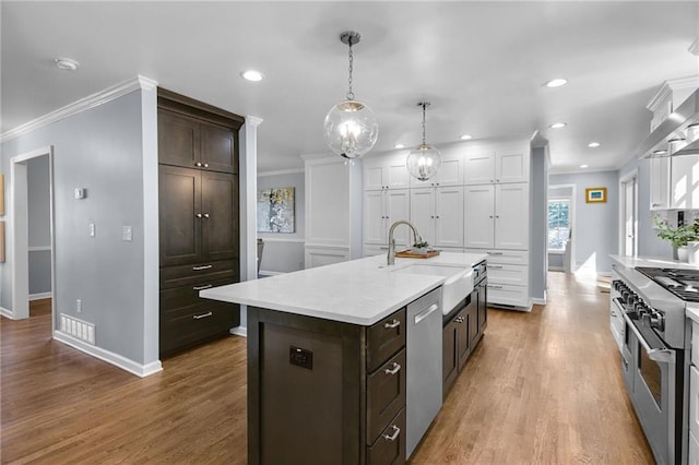 kitchen with sink, appliances with stainless steel finishes, hanging light fixtures, ornamental molding, and a center island with sink