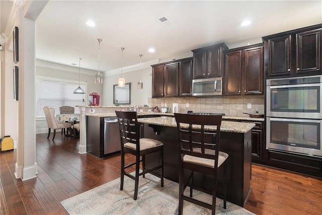 kitchen with kitchen peninsula, stainless steel appliances, decorative light fixtures, a breakfast bar, and a center island