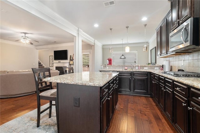 kitchen with decorative light fixtures, dark wood-type flooring, stainless steel appliances, tasteful backsplash, and a kitchen breakfast bar