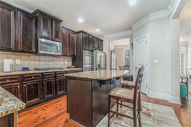 kitchen featuring dark wood-type flooring, light stone countertops, stainless steel appliances, and a center island