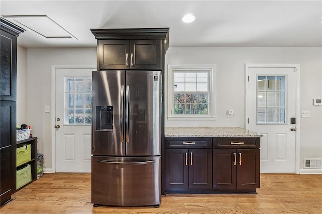 kitchen featuring light stone countertops, visible vents, light wood finished floors, dark brown cabinetry, and stainless steel refrigerator with ice dispenser