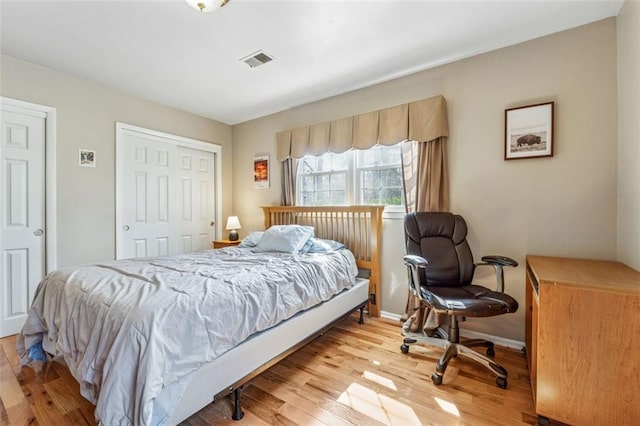 bedroom with light wood-type flooring, visible vents, baseboards, and a closet