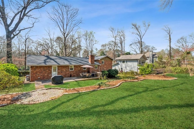 rear view of house with brick siding, a lawn, a chimney, and a patio area
