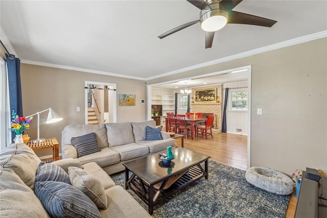living room with ornamental molding, ceiling fan with notable chandelier, and wood finished floors