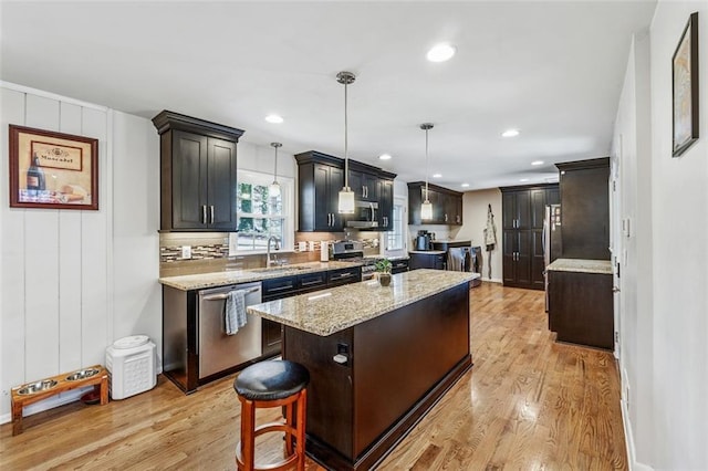 kitchen with light wood finished floors, a kitchen island, light stone counters, stainless steel appliances, and a sink