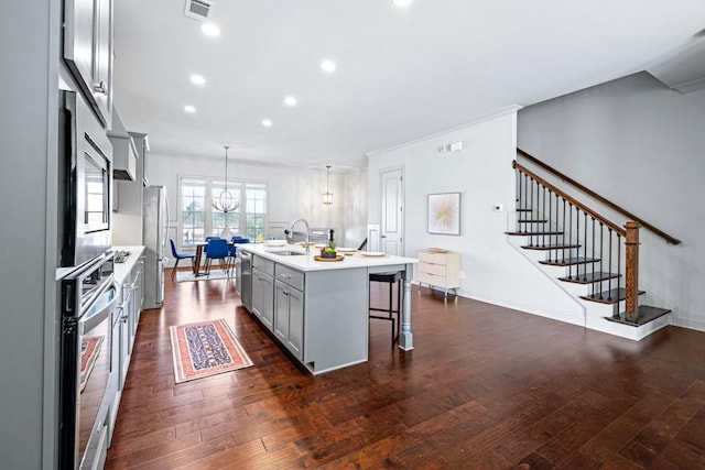 kitchen with a breakfast bar, dark wood finished floors, light countertops, appliances with stainless steel finishes, and a sink