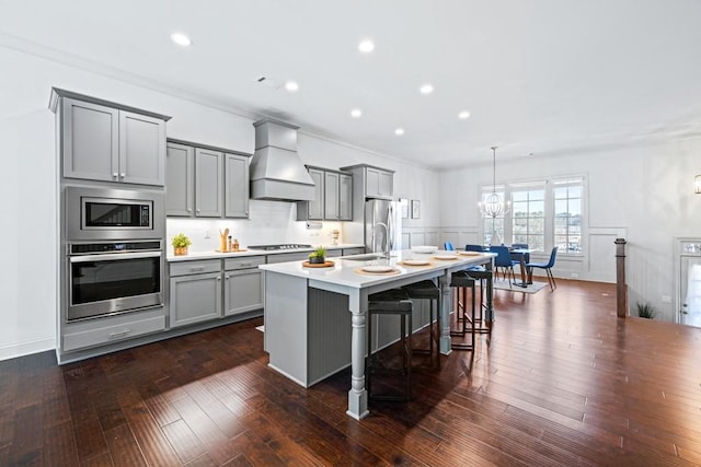 kitchen featuring a kitchen island with sink, gray cabinets, custom exhaust hood, and stainless steel appliances