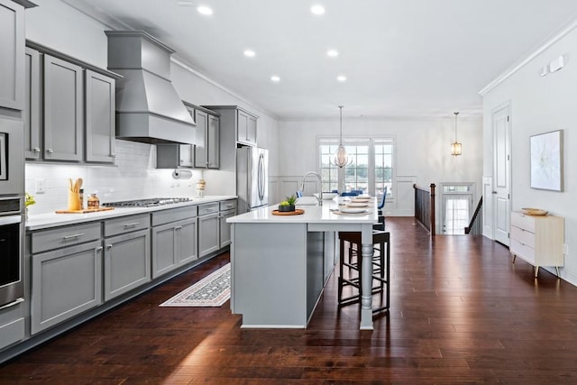 kitchen with a breakfast bar area, gray cabinetry, stainless steel appliances, ornamental molding, and custom range hood