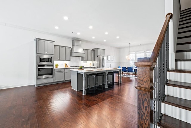 kitchen featuring gray cabinetry, stainless steel appliances, light countertops, a center island with sink, and custom range hood