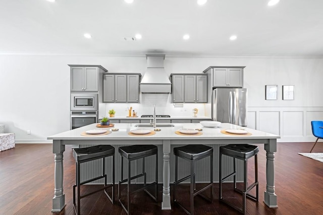 kitchen featuring an island with sink, premium range hood, stainless steel appliances, and gray cabinetry