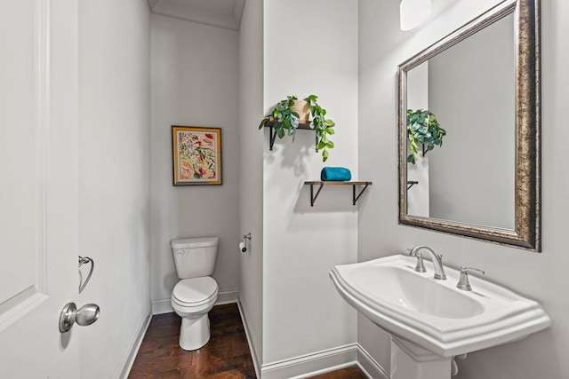 half bath with a sink, wood finished floors, toilet, and baseboards